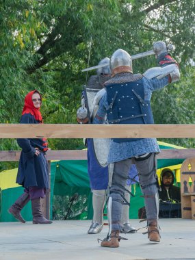 Tver / Rusya - 29 Eylül 2020: Ağır zırhlı savaşçılar kılıçlarla savaşıyor. Arka planda, hakem ve seyirciler. Ortaçağ Avrupa şövalye turnuvalarının tarihi yeniden yapılandırması