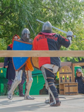 Tver / Rusya - 29 Eylül 2020: Ağır zırhlı savaşçılar kılıçlarla savaşıyor. Arka planda, hakem ve seyirciler. Ortaçağ Avrupa şövalye turnuvalarının tarihi yeniden yapılandırması