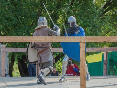 Tver / Rusya - 29 Eylül 2020: Ağır zırhlı savaşçılar kılıçlarla savaşıyor. Arka planda, hakem ve seyirciler. Ortaçağ Avrupa şövalye turnuvalarının tarihi yeniden yapılandırması