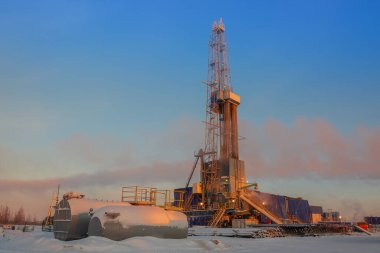 View of a drilling rig for drilling oil and gas wells in the rays of the rising sun. Winter polar day in the arctic. The sun colors everything orange clipart
