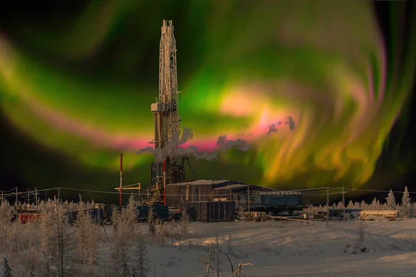 Winter landscape at polar night with a drilling rig. Northern oil and gas field. In the background there is a beautiful sky with northern lights