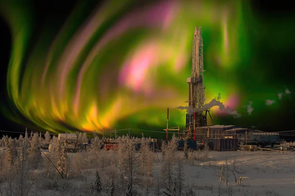 Winter landscape at polar night with a drilling rig. Northern oil and gas field. In the background there is a beautiful sky with northern lights