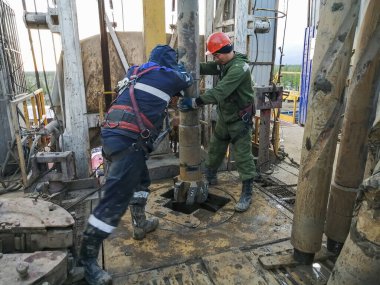 Nadym Rusya - 12 Haziran 2021: İki Asyalı sondaj işçisi kayaları delmek için petrol ve gaz kuyusuna PDC ucu yerleştirdi. Özel kıyafetler giyiyorlar, koruyucu miğfer takıyorlar. Teçhizatın içinde.