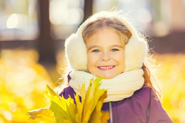 Menina feliz em earflaps com folhas de outono — Fotografia de Stock