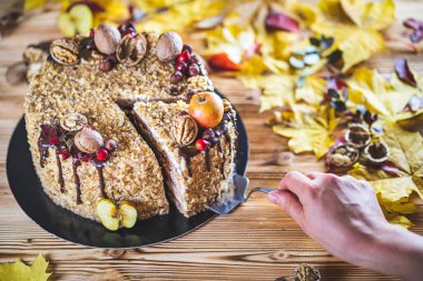 Kadın eli, çikolata soslu, cevizli ve elmalı tatlı ev yapımı pastayı ahşap sonbahar mahsulleri masasına koy.