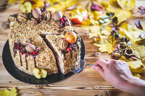 Kadın eli, çikolata soslu, cevizli ve elmalı tatlı ev yapımı pastayı ahşap sonbahar mahsulleri masasına koy.