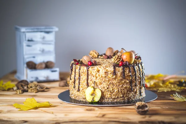 Çikolata soslu ev yapımı fındıklı kek ve ahşap şarap masasında ceviz ve elma. Sonbahar dekorasyonlu. Tatsız, sağlıksız tatlı manzaralı.
