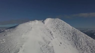 Güneşli Alpler 'de donmuş karlı dağın tepesinde uçmanın havadan görünüşü. Bulutlar ve buğulu engebeli arazi üzerindeki manzaralı dağ manzarası, kış doğasını ve dağ güzelliğini gözler önüne seriyor. İdeal