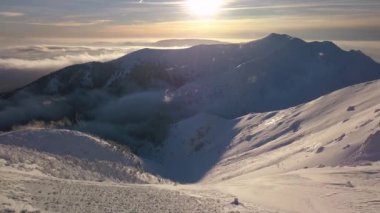 Güneşli bir gündoğumu sırasında Alpler 'in donmuş karlı zirvesinde dikilen bir adamın nefes kesici görüntüsü. Şaşırtıcı alp kış manzarası yumuşak bir geri dönüş insansız hava aracıyla çekildi..