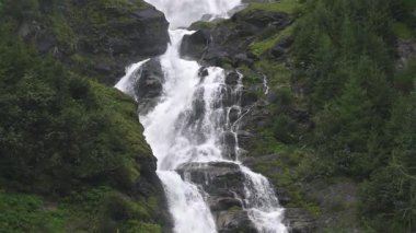 Büyük bir şelalenin yemyeşil orman dağlarındaki kayaların arasından yavaşça akması. Saf düşen su ve doğal akış, aşağı eğimli hareket manzaralı huzur dolu dağlık bir manzara..