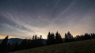Yıldızlı gece gökyüzünün yıldızlarla ve sessiz bir orman manzarasının üzerinde hızla sürüklenen bulutlarla birlikte astronomi zamanının uzaması. Gece doğası ve astronomi projeleri için mükemmel atmosfer arkaplanı.