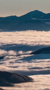 Foggy clouds flowing through a mountain valley like a river at sunrise. Warm morning light and drifting mist create a breathtaking, serene nature. Vertical panoramic time-lapse, natural background.