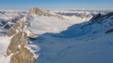 Kitzsteinhorn 'dan görülen Alplerdeki Kaprun kayak merkezinin geniş panoramik manzarası. Karlı dağlarla kaplı güneşli dağ manzarası, kış tatili, kayak ve tatil atmosferini yakalıyor..