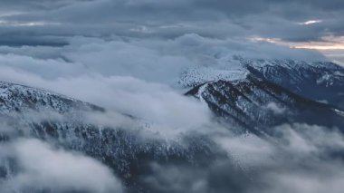 Kışın karlı bir dağlık vadide sürüklenen dramatik sis bulutlarının manzarası. Gri bulutlu puslu, gizemli atmosfer, dağlık yabanın mistik güzelliğini arttırır.