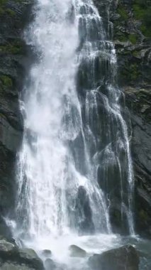 Dik çekimde, tatlı dağ suyunun doğal bir şelalede koyu kayaların üzerinde akması. Huzurlu doğa detayı, akan su dokularını ve ferahlatıcı açık havayı vurguluyor.