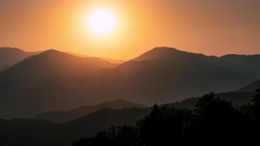 Altın bir yaz günbatımının dağların ve vahşi doğanın üzerinde, günden geceye geçişi. Sıcak güneş ışığı, renkli gökyüzü ve doğada sakin bir akşam atmosferi olan sakin doğal manzara..