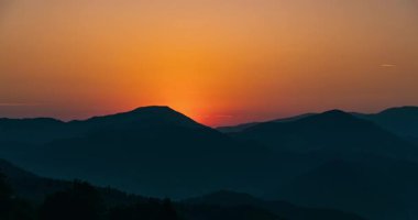 Güneşin dağların ardında yükselmesi, sakin doğa manzarasına altın ışığı yansıtıyor. Canlı turuncu gökyüzü ve renkli doğal manzaralı sihirli sabah atmosferi.