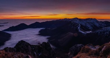 Bahar dağlarının başında huzurlu bir güneşin doğuşunun panoramik zamanlaması. Vadide sisli bulutlar akıyor. Altın güneş ışınları şafak vakti renkli bir gökyüzünü aydınlatırken. Mavi saatten geçerek.