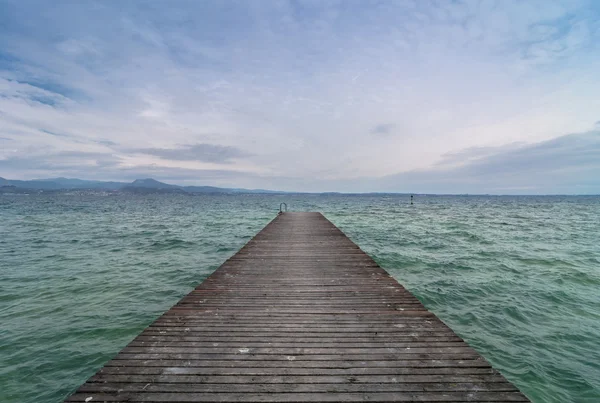 Dřevěné molo a zamračená obloha nad jezero Garda - Itálie — Stock fotografie