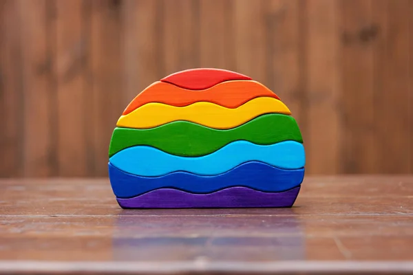 Wooden handcrafted wavy stacking toy painted in rainbow colors. Seven elements handmade puzzle play thing for toddlers. Front view natural material waldorf toys on brown background