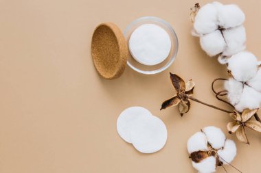 Cotton pads for removing makeup and branch of cotton plant on beige background, flat lay. Eco friendly concept. Skin care background. Copy space.