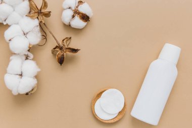 Cotton pads for removing makeup, cosmetic product and branch of cotton plant on beige background, flat lay. Eco friendly skin care concept. Cosmetic background. Copy space.