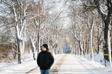 Karlı yolun arka planında siyah ceketli genç adamın portresi. Tek başına seyahat konsepti. Yaşam biçimi.