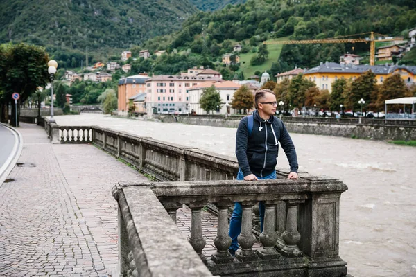 Young man solo travels around Europe, looking at river in one of small towns.