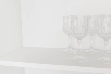 Bulaşıklar mutfakta. Şeffaf cam şarap kadehi, mutfak dolabındaki beyaz bir rafta duruyor. Seçici odak.