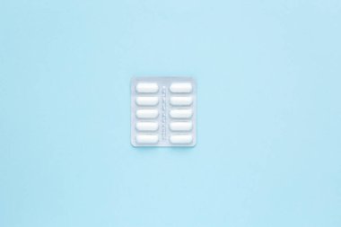 Minimalizm. Mavi arka planda beyaz kapsül ve ilaç paketleri. Ağrı kesici. Tıp konsepti. Boşluğu kopyala.