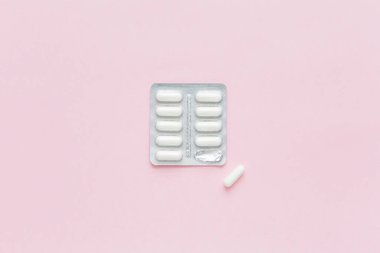 Pembe arka planda ilaç içeren beyaz kapsüller. Kadın Sağlığı. Doğum kontrol hapları. İlaç rejimi.