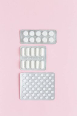 Pembe arka planda ilaç içeren beyaz haplar ve kapsüller. Kadın Sağlığı. Hastalık önleme.