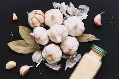 Kavanozda kurutulmuş sarımsak ve baharatlı aromatik sarımsak soğanları, defne yaprağı ve karabiberli, siyah arka planda..
