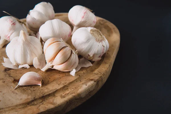 Garlic bulbs on wooden board, on black background. Natural antibiotic. Growing vegetables, farming.