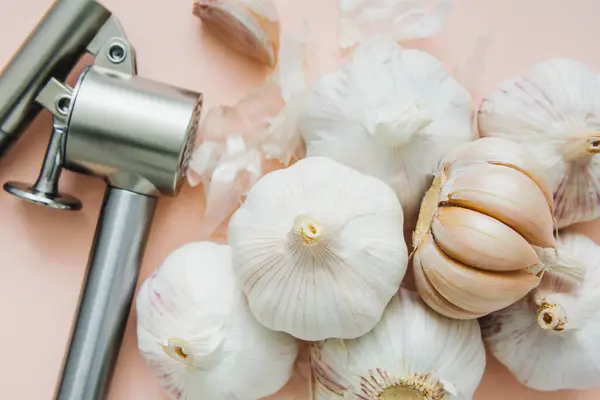 Garlic bulbs and garlic press on pink background, close-up. Organic garlic top view. Food background. Selective focus.
