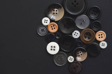 Siyah arka planda farklı boyutlarda birçok yuvarlak düğme, üst görünüm. Dikiş ve dikiş konsepti. El işi malzemeleri mağazası..