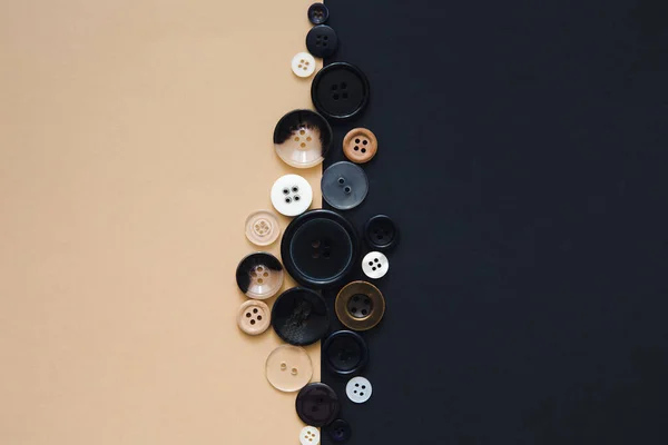 Sewing and handmade concept. Many round sewing buttons of different sizes on a beige and black background, top view. Needlework and hobby background.