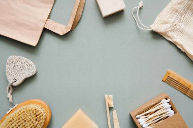 Doğal banyo aksesuarları: tahta diş fırçaları, bambu kulak çubukları, organik sabun, yeşil arka planda yeniden kullanılabilir pamuk torbaları. Sıfır atık alışveriş, çevre dostu yaşam tarzı, plastiksiz.
