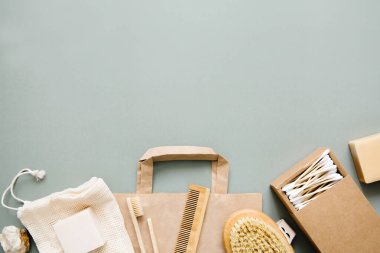 Doğal banyo aksesuarları: tahta diş fırçaları, bambu kulak çubukları, organik sabun, yeşil arka planda yeniden kullanılabilir pamuk torbaları. Sıfır atık alışveriş, çevre dostu yaşam tarzı, plastiksiz.