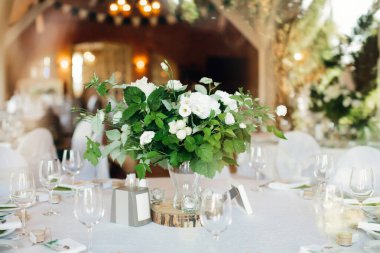 Yeşillikli bir buket beyaz çiçek, şenlikli akşam yemeği için masa süsü olarak. Düğün ya da doğum günü onuruna bir kutlama. Seçici odak.