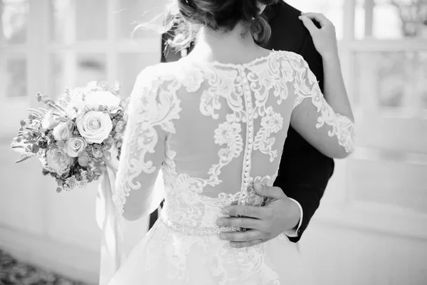 Siyah beyaz fotoğrafçılık. Damat geline, belinde beyaz bir elbise ile sarılıyor. Erkek el yakın çekim. Seçici odak.