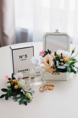 Gelinin sabahı. Bir şişe Chanel No. 5 parfüm, bir yaka çiçeği ve yuvarlak beyaz bir masada alyans..