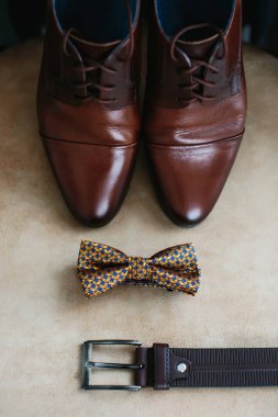 Kahverengi erkek ayakkabıları hakiki deriden, kemer ve bej arka planda papyon, yakın plan. Damat sabahı. Seçici odak.