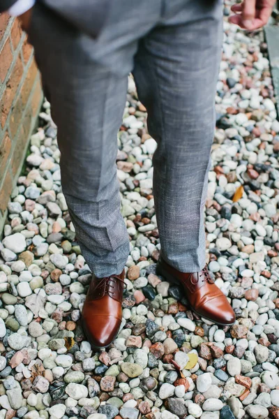 Man in a gray suit and brown shoes stands on stone surface. Male feet in brown leather shoes close up. Selective focus.