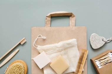 Natural bathroom accessories: wooden toothbrushes, bamboo ear sticks, organic soap, reusable cotton bags on a green background. Zero waste shopping, eco-friendly lifestyle, plastic free.