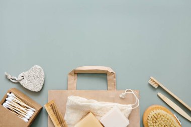 Doğal banyo aksesuarları: tahta diş fırçaları, bambu kulak çubukları, organik sabun, yeşil arka planda yeniden kullanılabilir pamuk torbaları. Sıfır atık alışverişi, çevre dostu yaşam tarzı, plastiksiz. Boşluğu kopyala.
