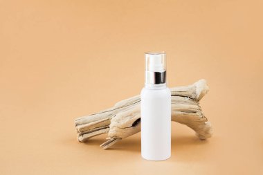 Beyaz kozmetik konteynır ve bej arka planda kuru bir ahşap dal. Çevre dostu kozmetik üretimi kavramı. Doğal kozmetik. Düzen, kopyalama alanı.