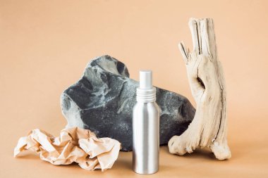 Metalik kozmetik konteynır bir taşın arka planında ve ahşap bir dalda. Çevre dostu kozmetik üretimi kavramı. Doğal kozmetik. Tasarım için düzenName.