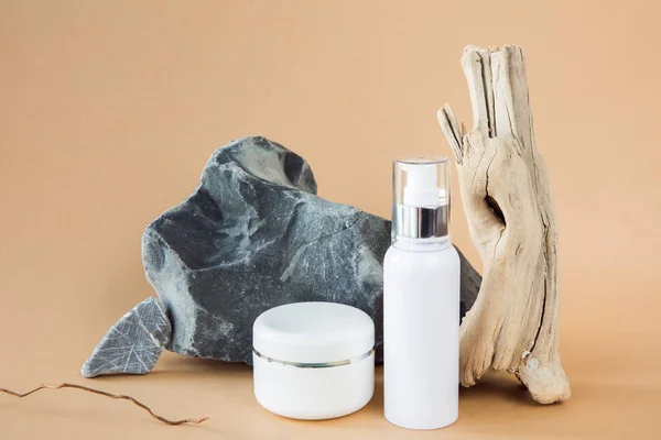 Untitled white cosmetic containers on a background of a stone and a wooden branch. The concept of environmentally friendly production of cosmetics. Natural cosmetic. Layout for design.