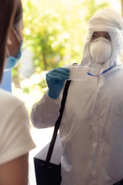 Medical staff in PPE suit show his ID card to patient to identified himself at home before doing swab for COVID-19 at home delivery. Delivery coronavirus covid-19 test at home concept.